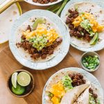 three chorizo, scrambled eggs, avocado tacos on white plates