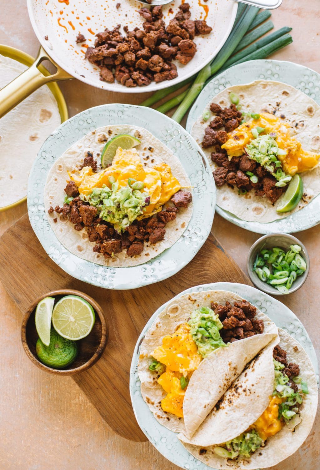 three chorizo, scrambled eggs, avocado tacos on white plates