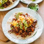 chorizo and egg taco with avocado and hot sauce on white plate