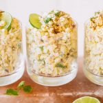 Mexican corn in a cup topped with cotija cheese, chili powder and a lime wheel.