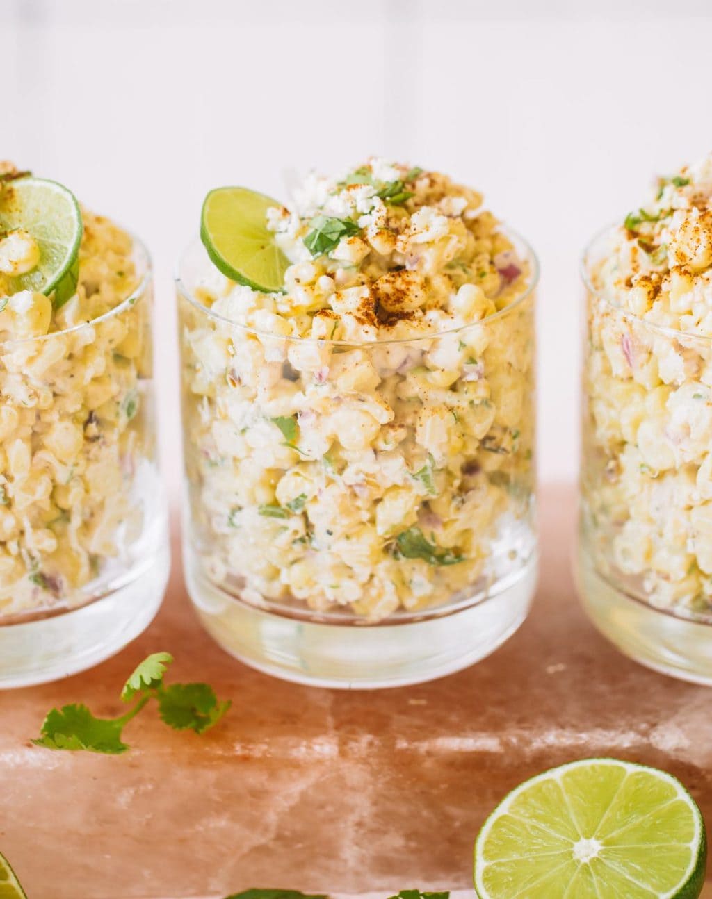 Mexican corn in a cup topped with cotija cheese, chili powder and a lime wheel.