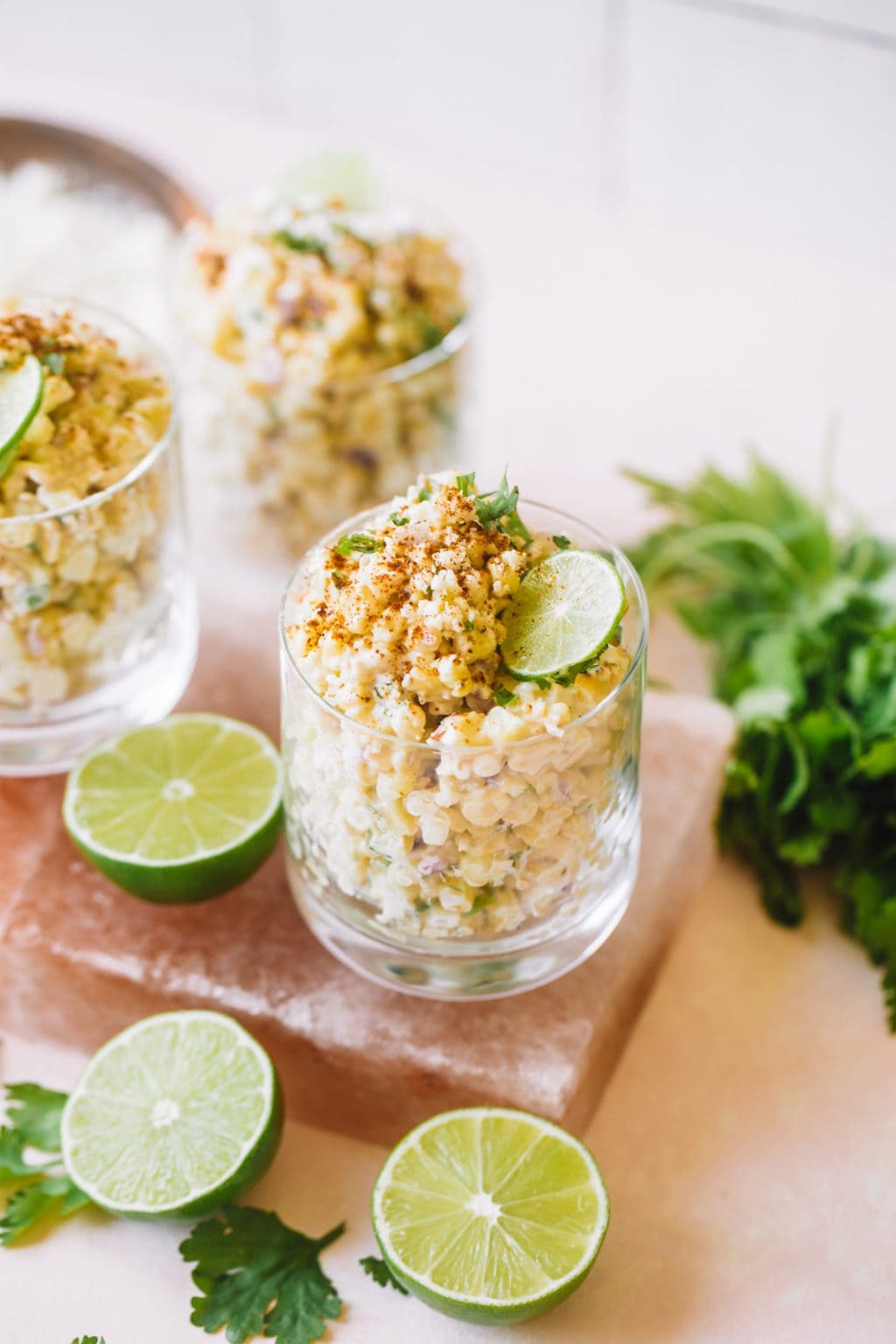 Mexican corn in a cup topped with cotija cheese, chili powder and a lime wheel.