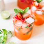 Strawberry gin mojito poured in a low ball glass topped with ice cubes, strawberries and fresh mint.
