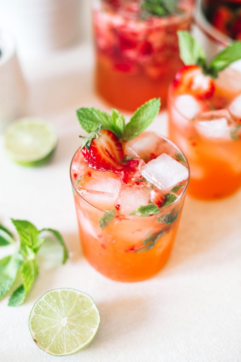 Strawberry gin mojito poured in a low ball glass topped with ice cubes, strawberries and fresh mint.