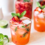 Strawberry gin mojito poured in a low ball glass topped with ice cubes, strawberries and fresh mint.