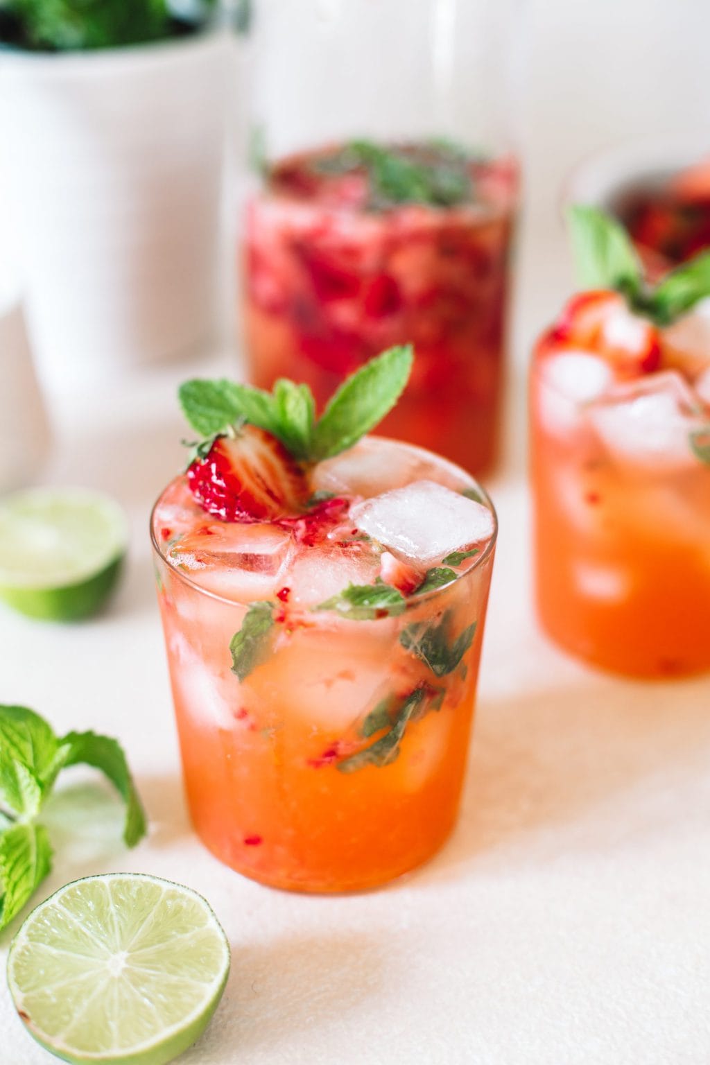 Strawberry gin mojito poured in a low ball glass topped with ice cubes, strawberries and fresh mint.