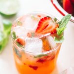 Strawberry gin mojito poured in a low ball glass topped with ice cubes, strawberries and fresh mint.