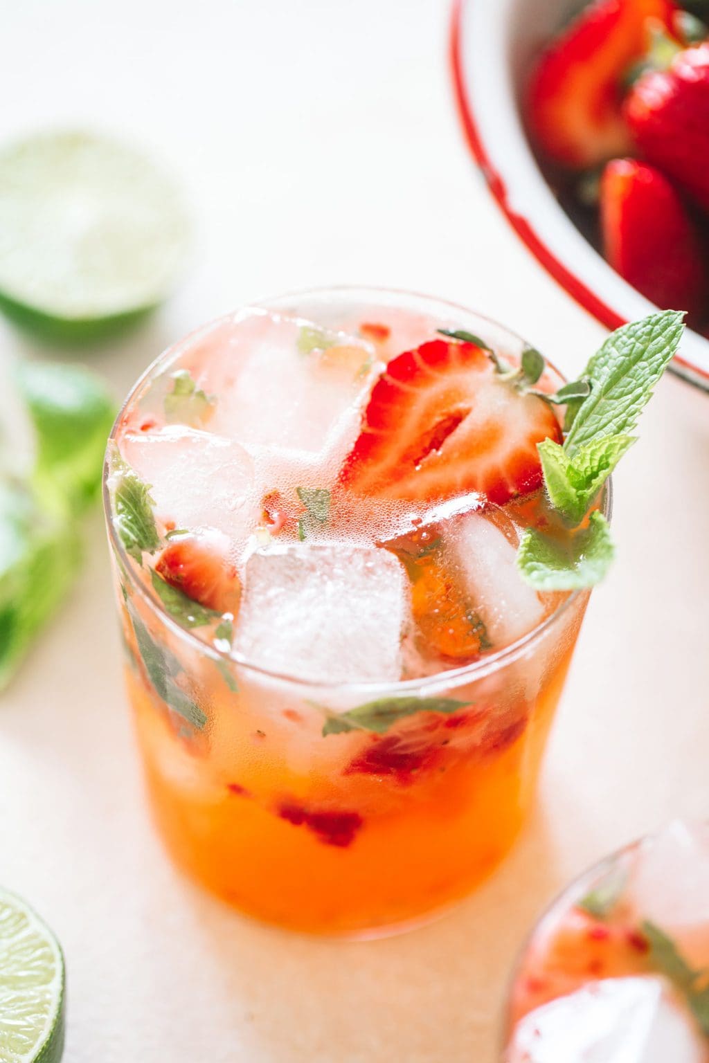 Strawberry gin mojito poured in a low ball glass topped with ice cubes, strawberries and fresh mint.