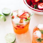Strawberry gin mojito poured in a low ball glass topped with ice cubes, strawberries and fresh mint.