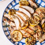 sliced lemon chicken recipe with lemon wheels on blue striped plate