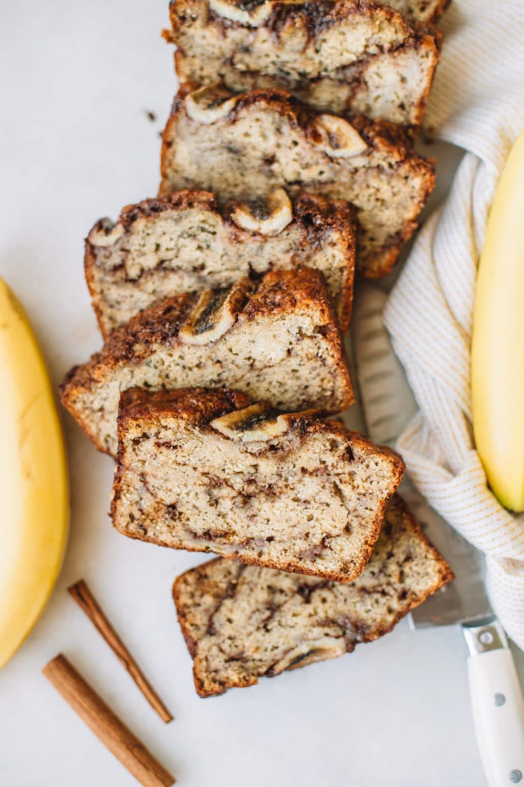 Cinnamon banana bread sliced in slices with bananas next to the slices.