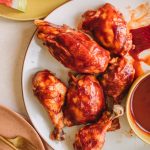 Platter of bbq chicken breasts, thighs and drumsticks with a side bowl of bbq sauce.