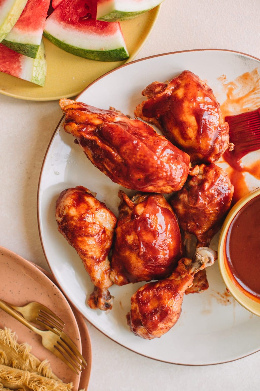 Platter of bbq chicken breasts, thighs and drumsticks with a side bowl of bbq sauce.