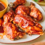 Platter of bbq chicken breasts, thighs and drumsticks with a side bowl of bbq sauce.