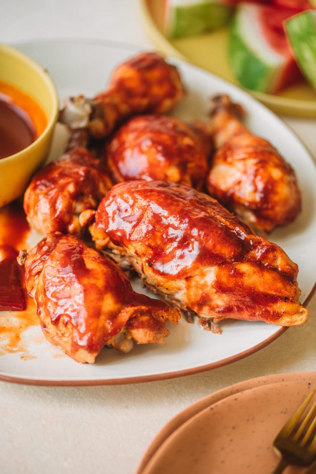 Platter of bbq chicken breasts, thighs and drumsticks with a side bowl of bbq sauce.