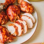 Platter of bbq chicken breasts, thighs and drumsticks with a side bowl of bbq sauce.