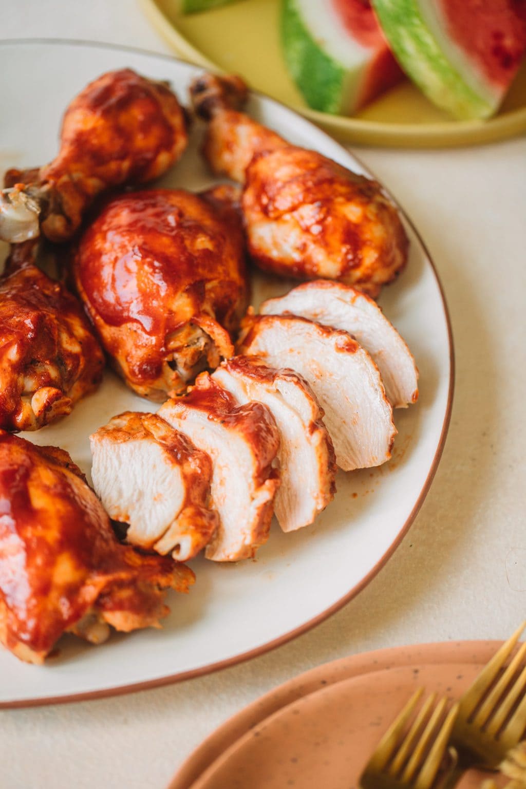 Platter of bbq chicken breasts, thighs and drumsticks with a side bowl of bbq sauce.