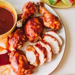 Platter of bbq chicken breasts, thighs and drumsticks with a side bowl of bbq sauce.