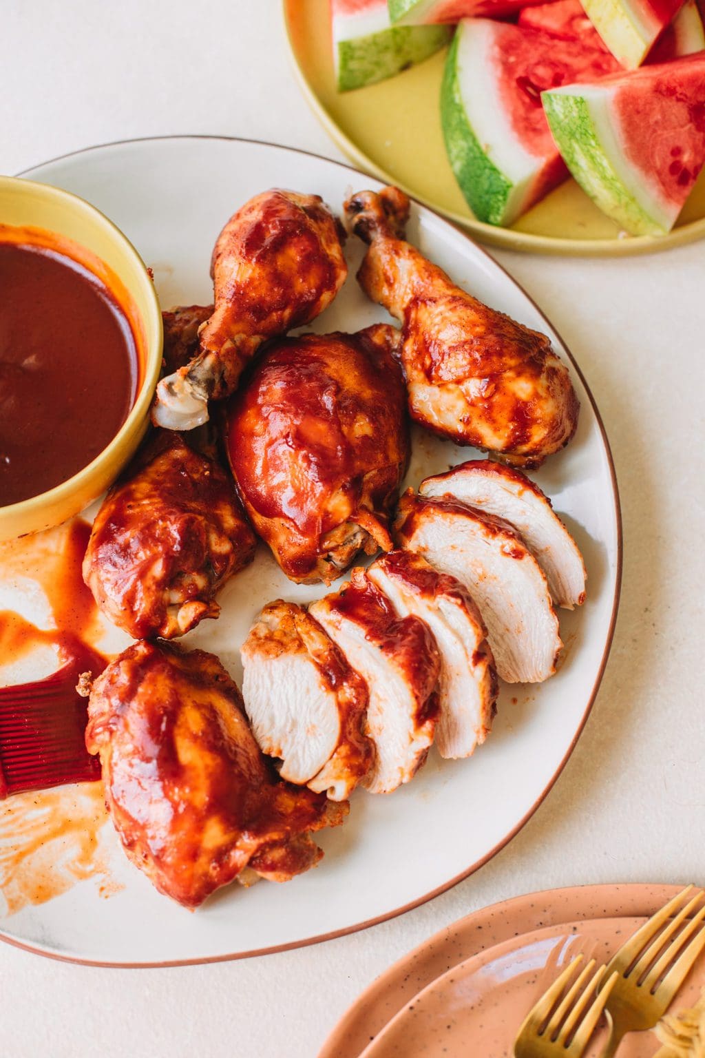 Platter of bbq chicken breasts, thighs and drumsticks with a side bowl of bbq sauce.