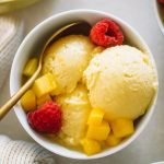 mango ice cream served in a small white dish topped with raspberries.