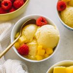 mango ice cream served in small white bowls with raspberries.