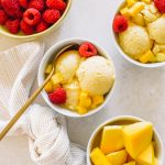 Mango ice cream served in small white bowls topped with raspberries.