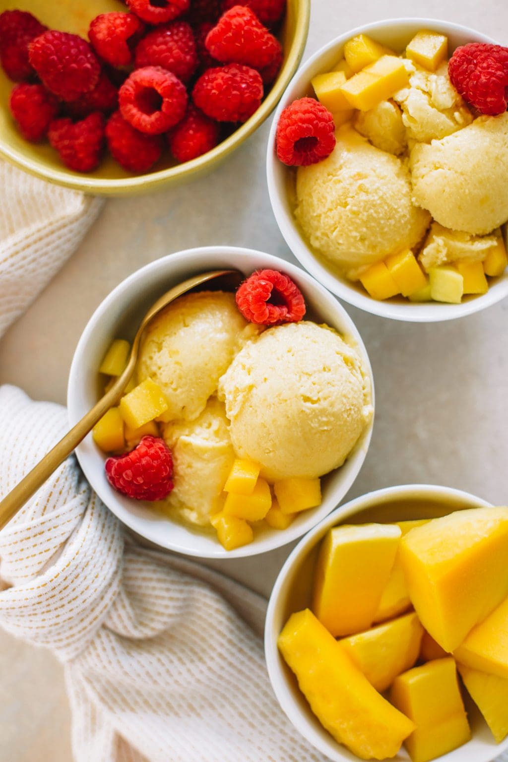 mango ice cream served in small white dishes topped with raspberries.