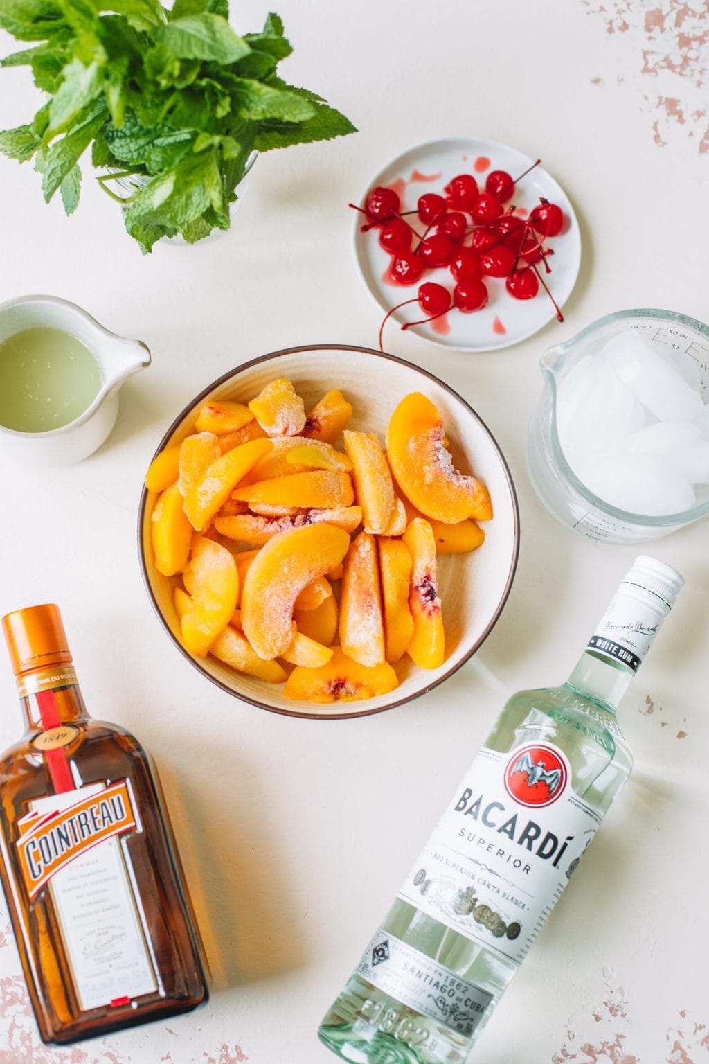 frozen peaches in white bowl, bacardi white rum, cointreau, lime juice, ice cubes, maraschino cherries