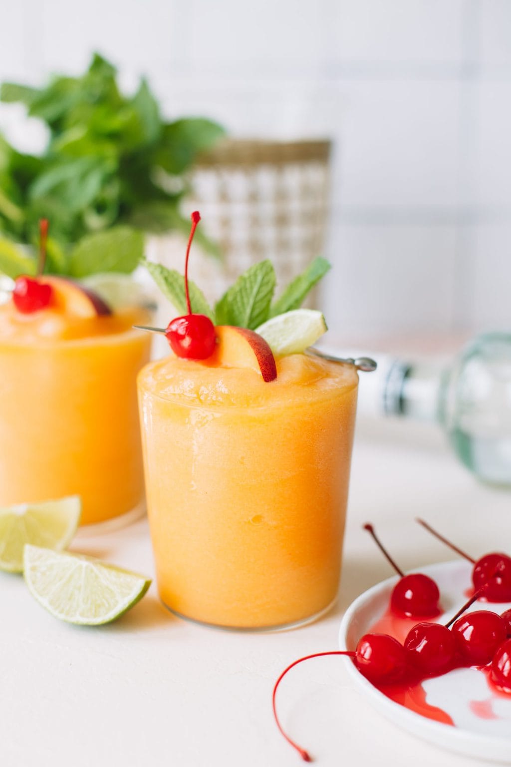 two frozen peach daiquiris with cherry and lime garnish in glasses