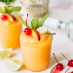 two frozen peach daiquiris with cherry and lime garnish in glasses