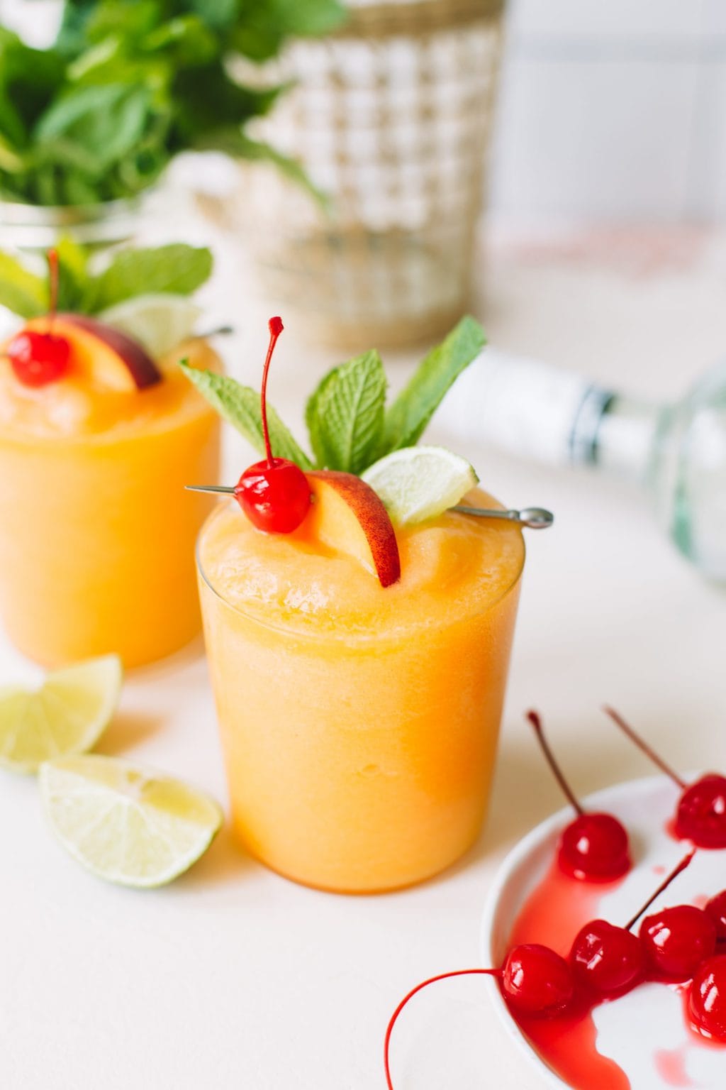 two frozen peach daiquiris with cherry and lime garnish in glasses