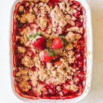 summer fruit crisp in white casserole dish topped with fresh strawberries