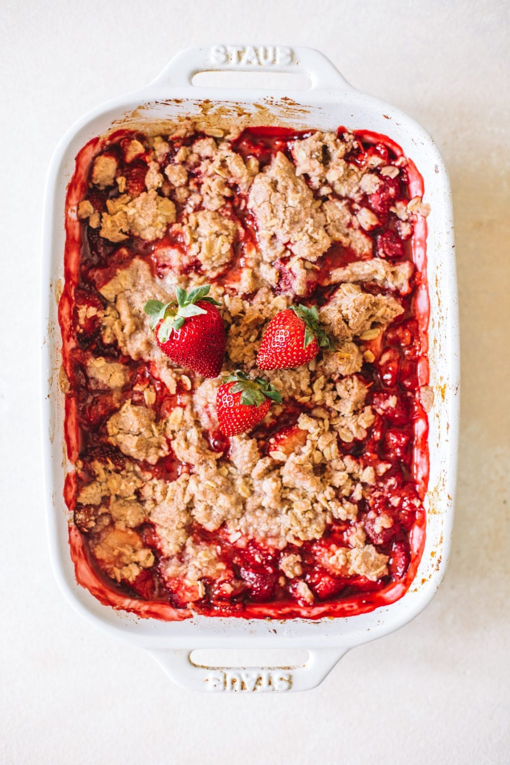 summer fruit crisp in white casserole dish topped with fresh strawberries