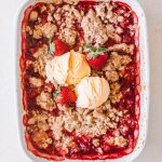 fresh strawberry crumble recipe in white casserole dish topped with vanilla ice cream