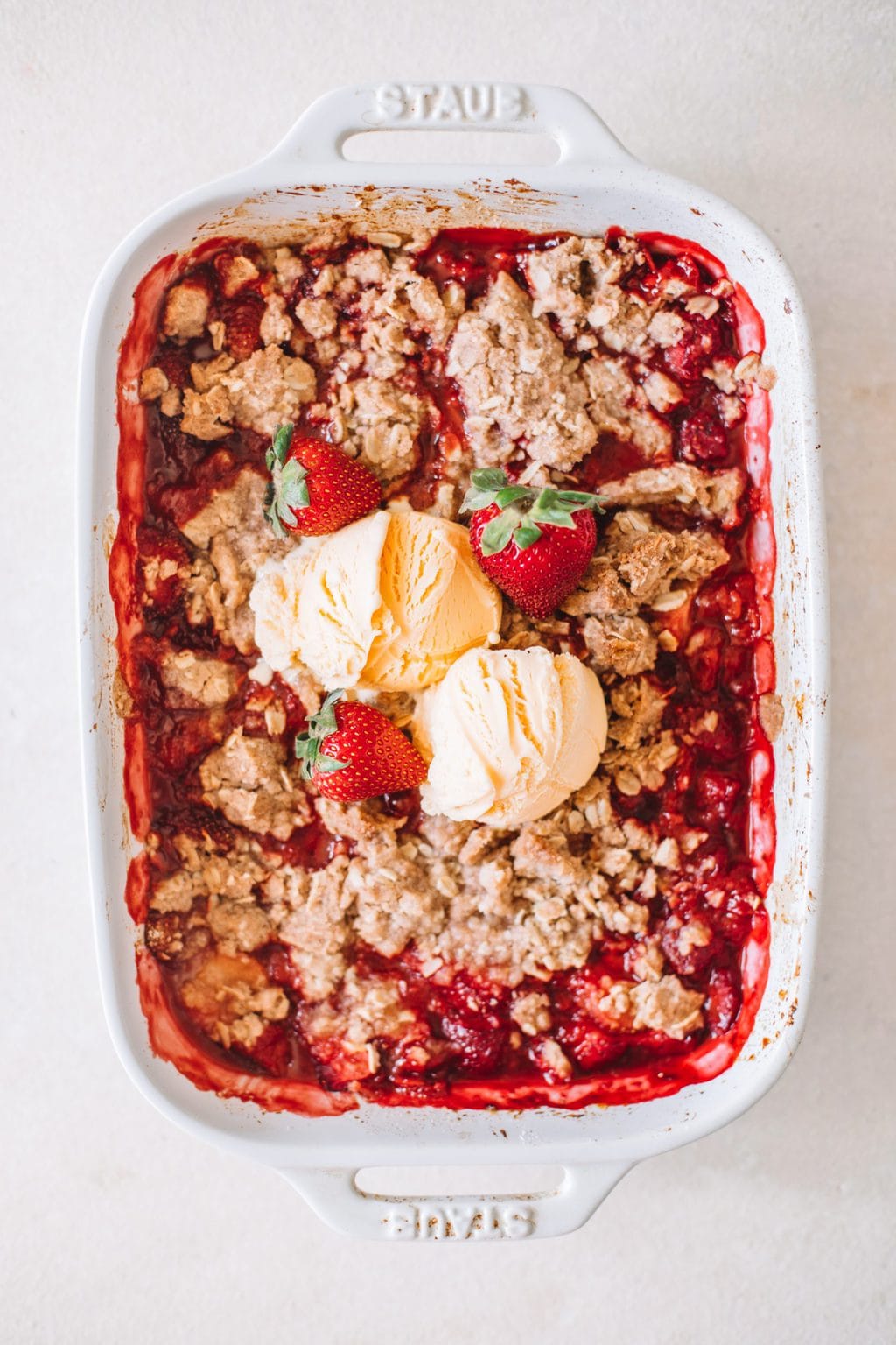 fresh strawberry crumble recipe in white casserole dish topped with vanilla ice cream