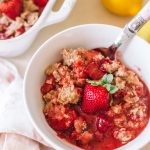 easy strawberry crumble recipe in white bowl with spoon and lemon on the side