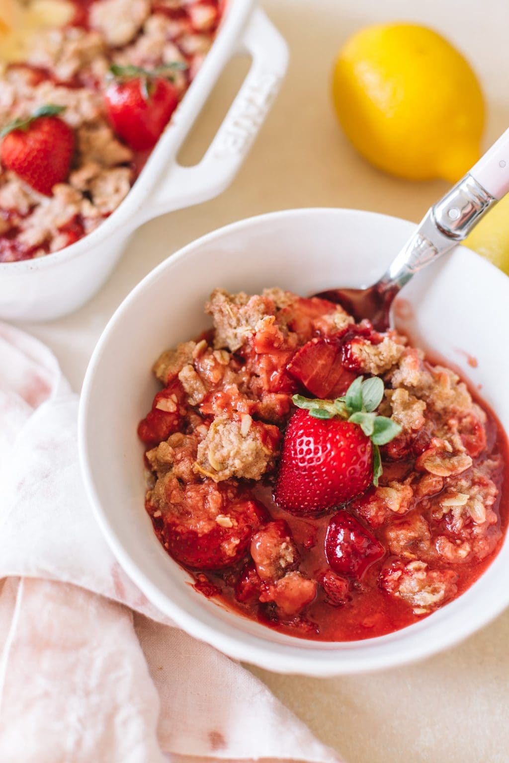 easy strawberry crumble recipe in white bowl with spoon and lemon on the side