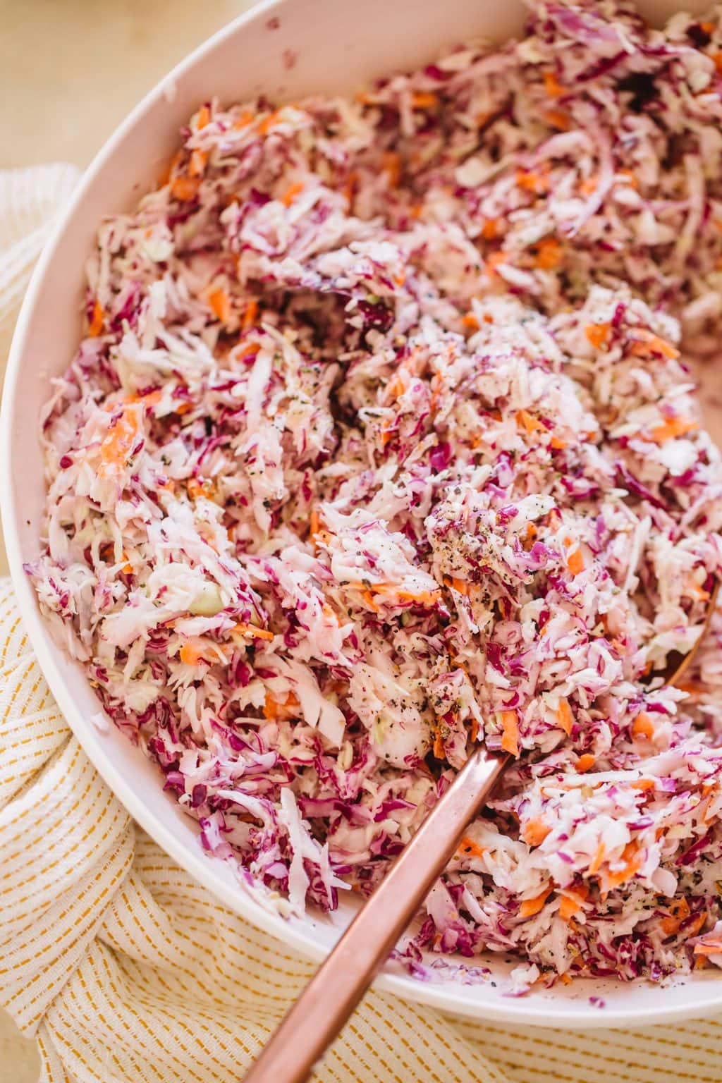 A pink bowl filled with vegan coleslaw with a copper serving spoon.