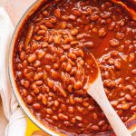 easy vegetarian baked beans in yellow dutch oven with wooden spoon and white kitchen towel