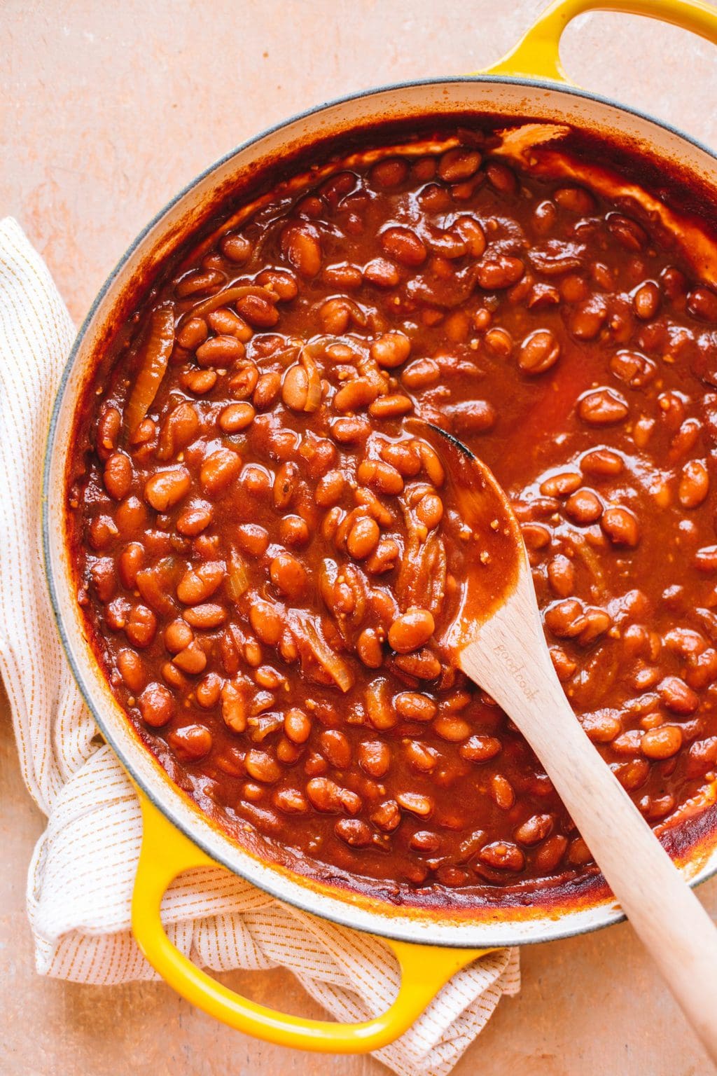 easy vegetarian baked beans in yellow dutch oven with wooden spoon and white kitchen towel