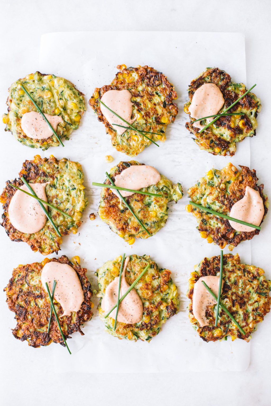 zucchini corn fritters on parchment paper topped with dipping sauce and chives