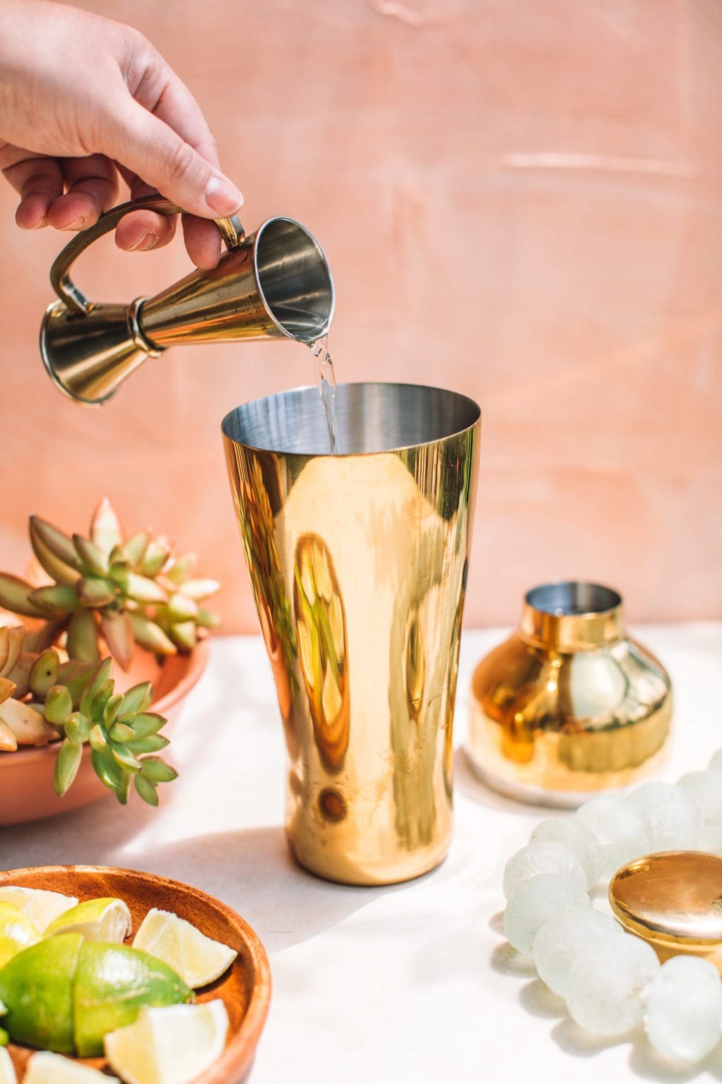 hand pouring liquor into gold cocktail shaker from one ounce pourer