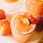 easy frozen peach cocktail recipe in glass with peach garnish