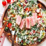 Kale Caesar Chopped Salad on a wooden plate with copper tongs.