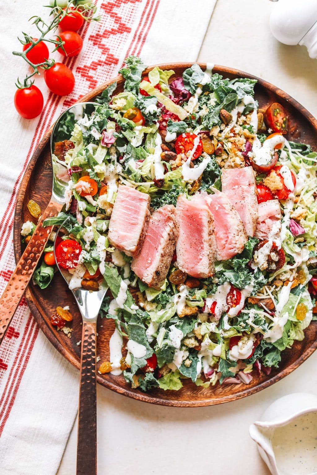 Kale Caesar Chopped Salad on a wooden plate with copper tongs.