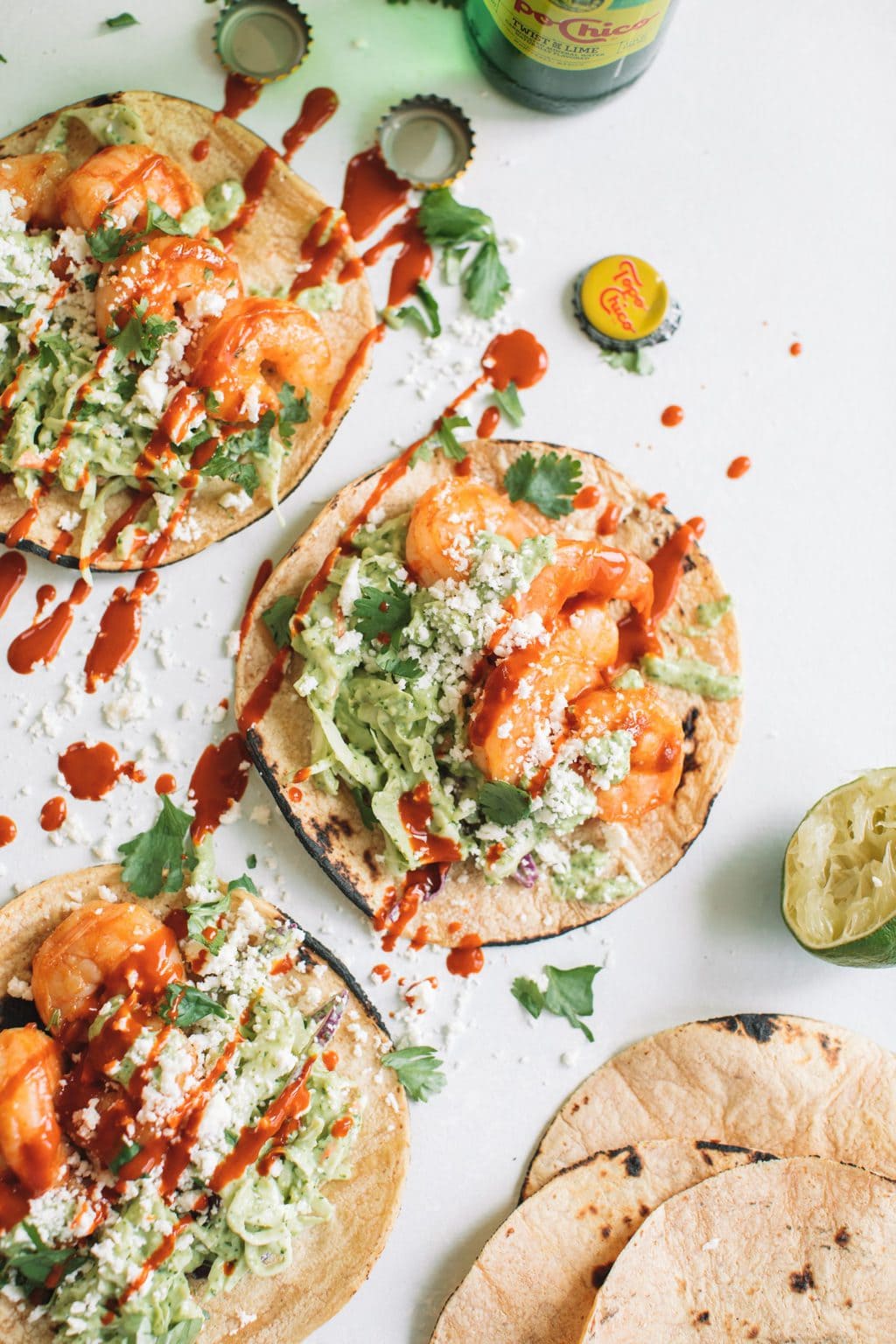 healthy shrimp taco recipe with avocado crema wrapped in corn tortillas on white surface