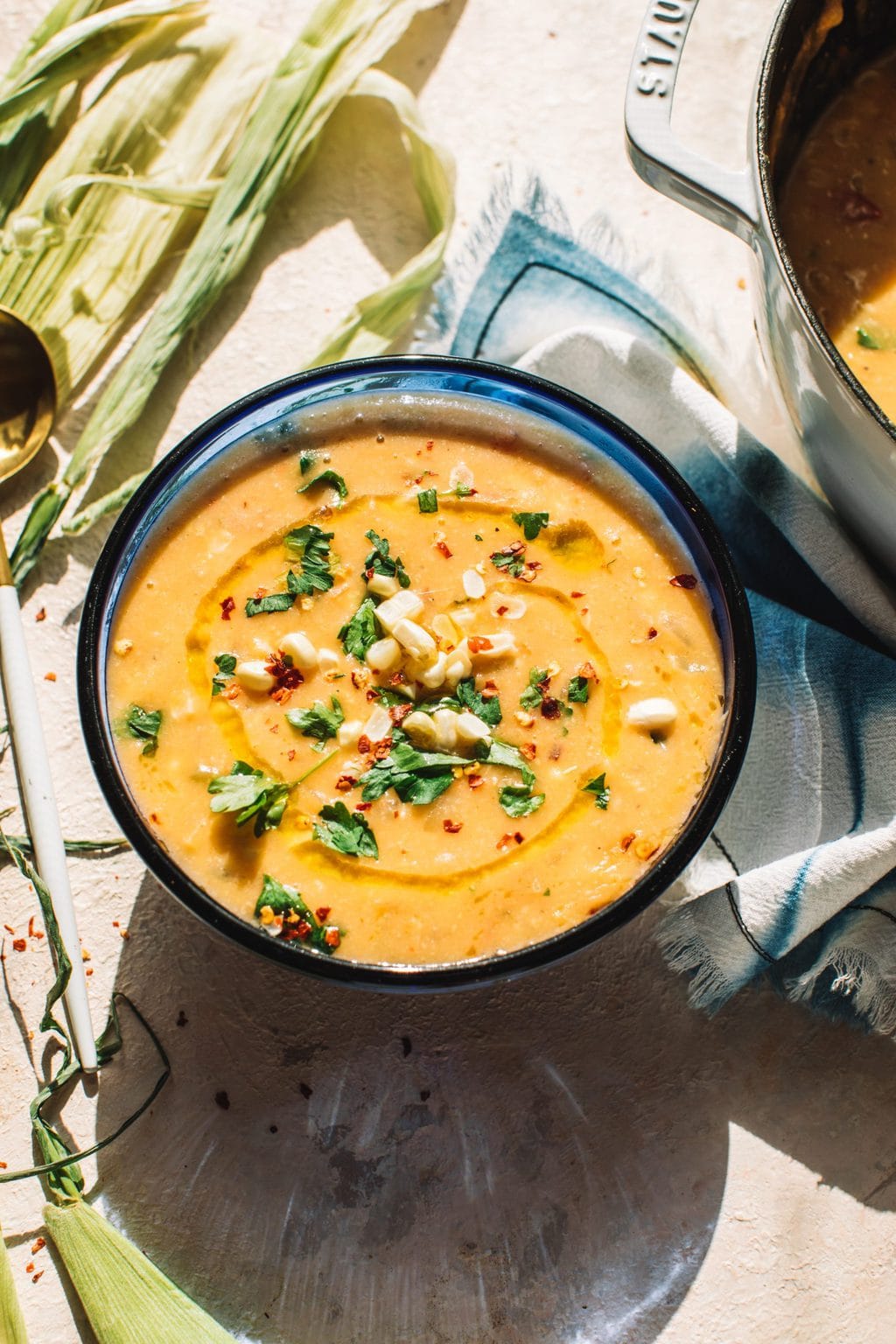 easy corn soup recipe in blue bowl garnished with fresh corn, chives and parsley on decorative kitchen towel