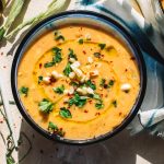 summer corn chowder in blue bowl garnished with fresh corn, chives and parsley on kitchen towel