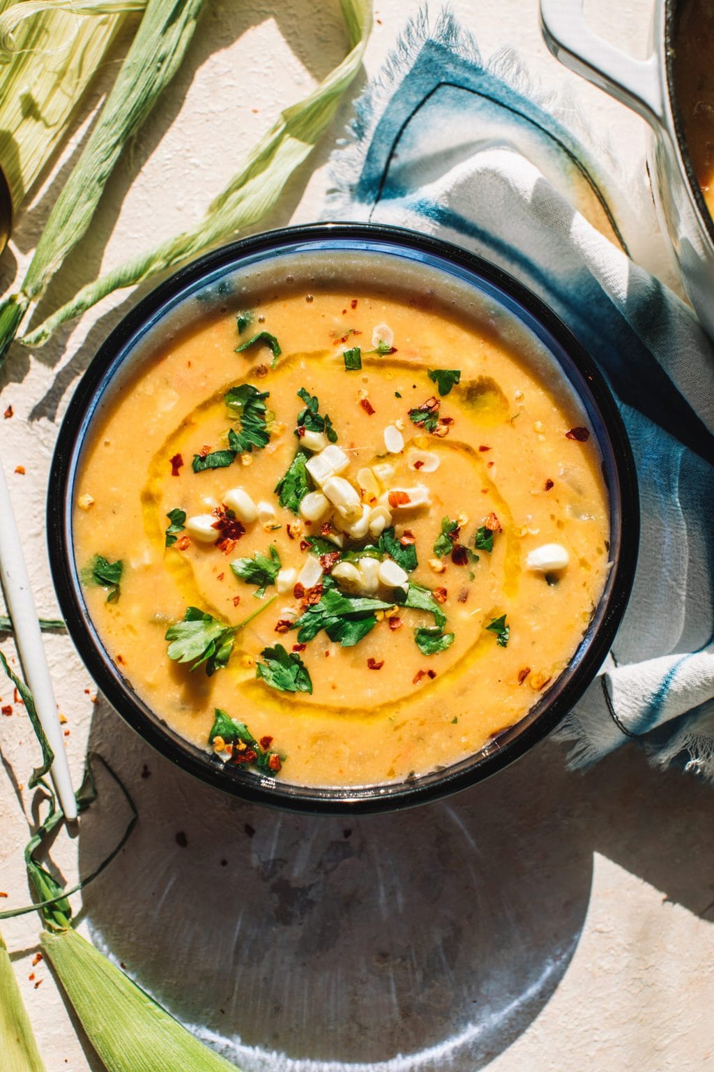 summer corn chowder in blue bowl garnished with fresh corn, chives and parsley on kitchen towel