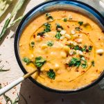 easy corn soup recipe in blue bowl garnished with fresh corn, chives and parsley with large gold spoon